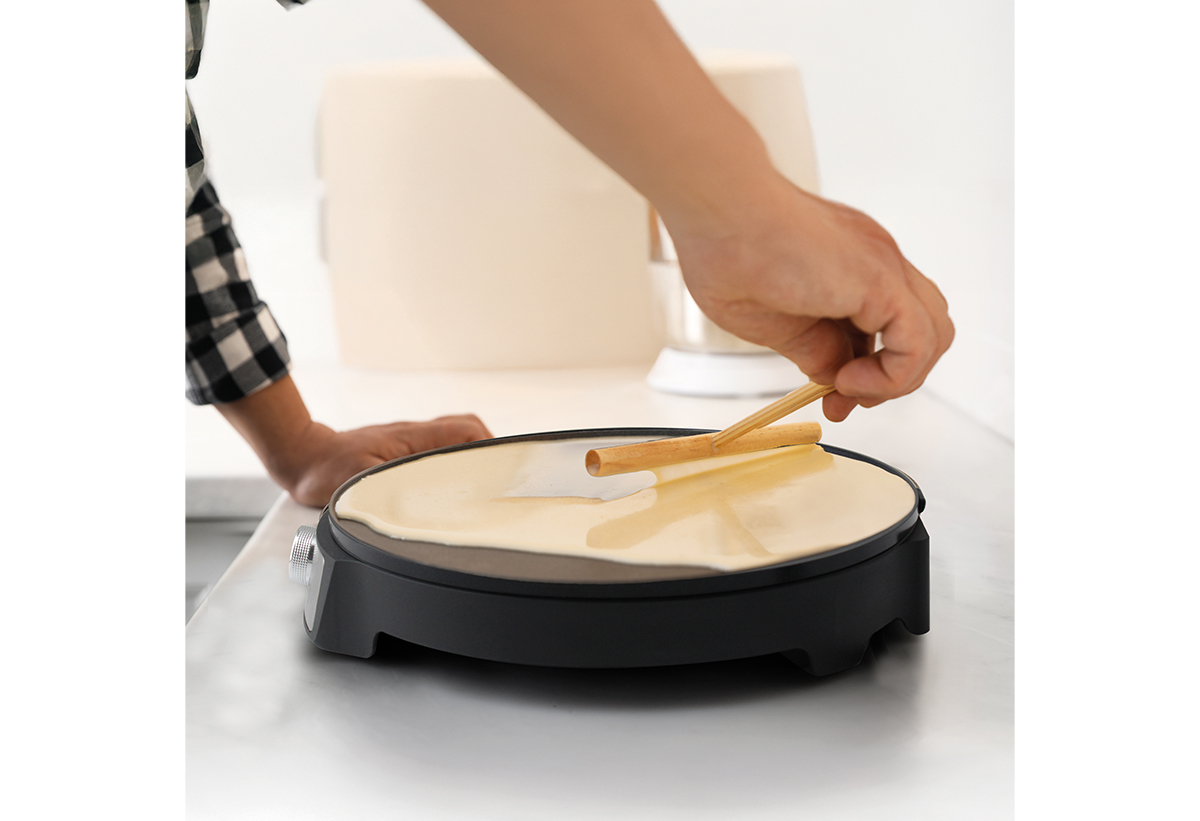 Ένα χέρι απλώνει μια κρέπα στην κρεπιέρα.